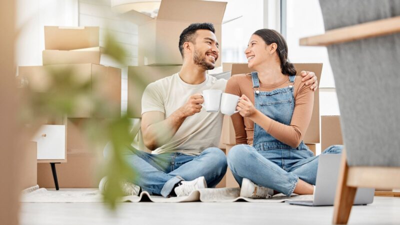 Happy couple, cheers and drinking coffee in new home to celebrate moving to apartment. Man, woman or toast with cup in property for real estate investment, success or relocate to dream house together